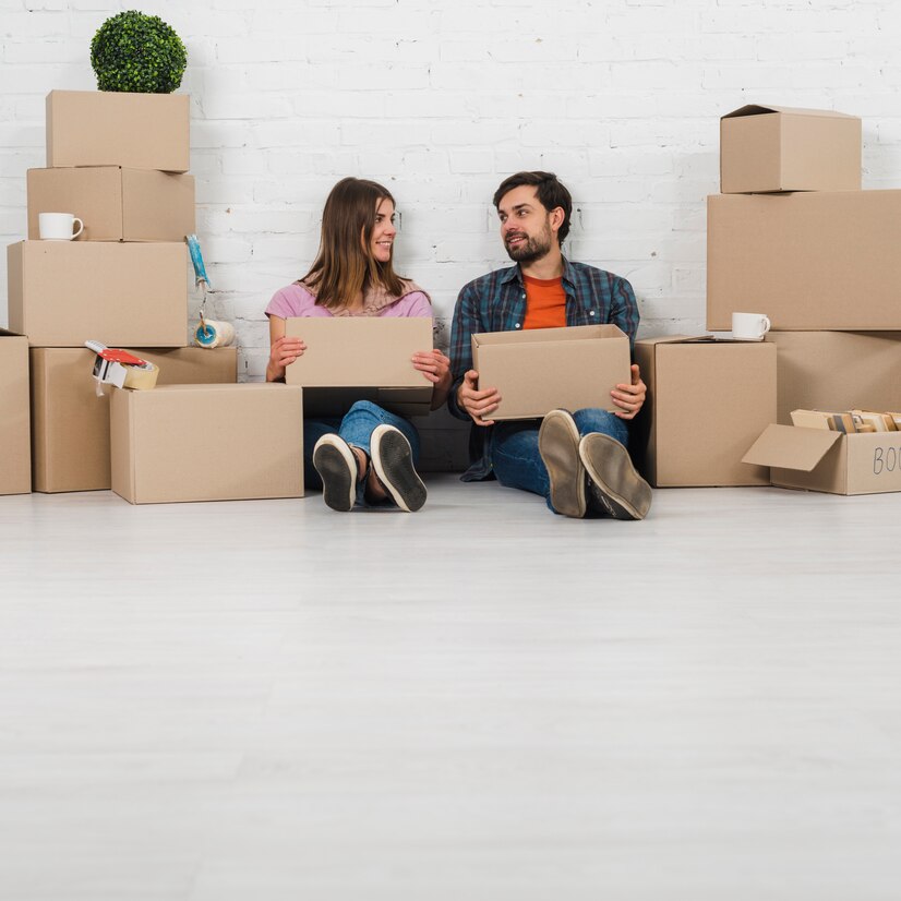 young-couple-sitting-floor-holding-cardboard-boxes-hand-looking-each-other_23-2148095464